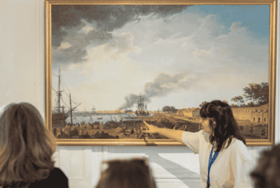Une guide pointe un élément sur un tableau représentant l'Arsenal de Rochefort
